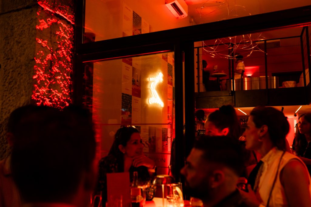 Soirée au rez-de-chaussée du Contrast : les invités attablés sous la mezzanine, dans une lumière rouge
